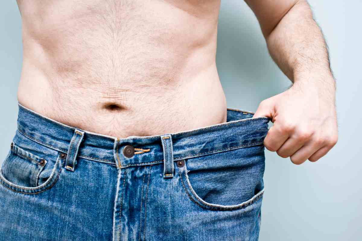 uomo che mostra il jeans di due taglie più grande dopo che si è impegnato a perdere peso velocemente