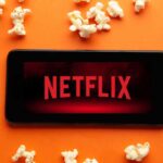 smartphone con logo netflix e pop corn su sfondo arancione