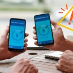 Due persone con due telefoni, uno che fa un bonifico e l'altro che lo riceve ed in alto a sinistra un segnale di pericolo