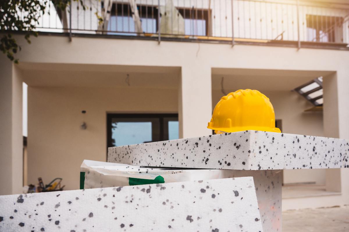 Il materiale per il cappotto termico di fronte ad una casa ed un elmetto per lavoratori 