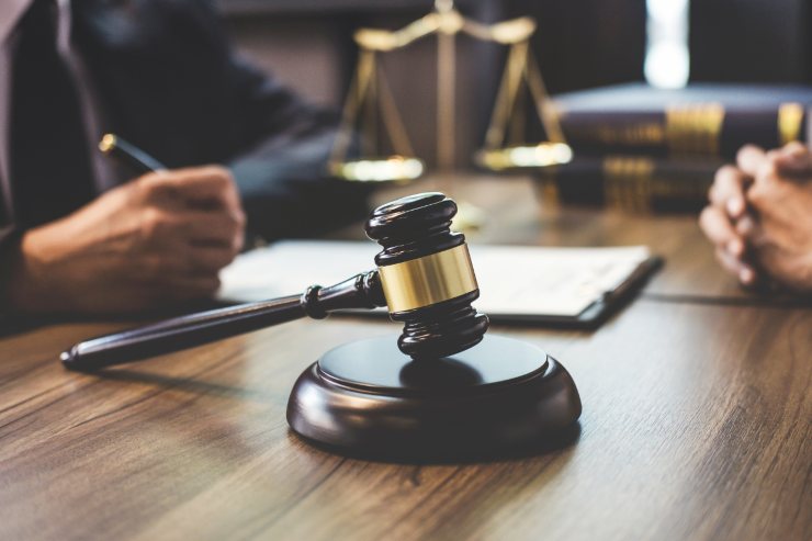 Un giudie che sta al lavoro con la bilancia di giustizia ad un suo lato ed un martello da giudice dall'altro lato