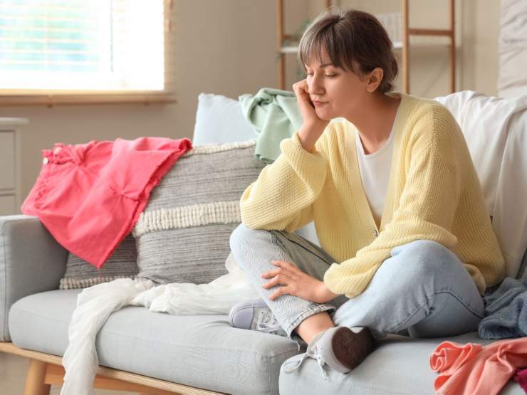 ragazza triste con vestiti sparsi per casa