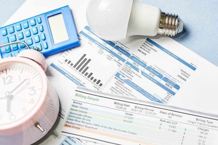 Delle bollette accumulate, una lampadina una calcolatrice ed una sveglia sul tavolo