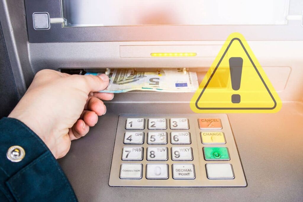 mano di donna che preleva contanti euro dallo sportello bancomat e segnale pericolo giallo