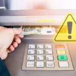 mano di donna che preleva contanti euro dallo sportello bancomat e segnale pericolo giallo