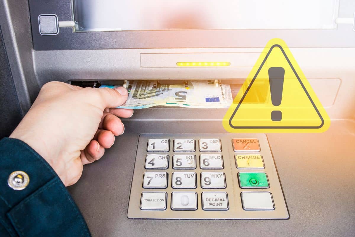 mano di donna che preleva contanti euro dallo sportello bancomat e segnale pericolo giallo