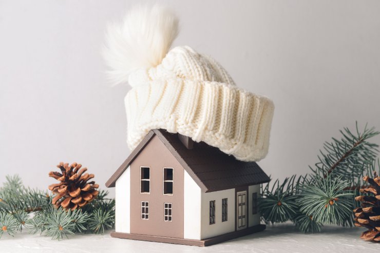 Una miniatura di una casa con sopra un cappello di lana ed attorno pigne e rami di pino per evidenziare la stagione invernale
