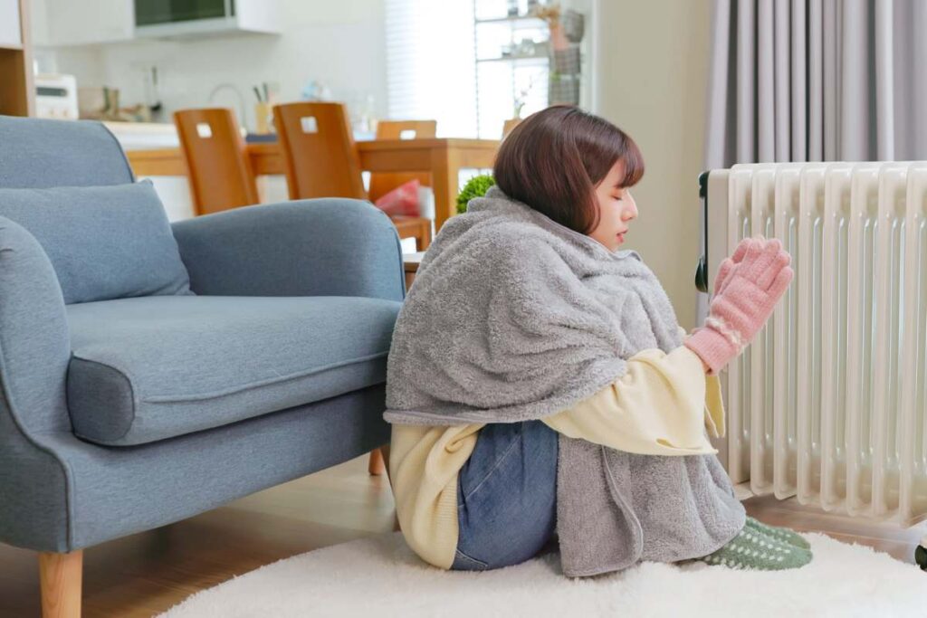 Una persona in casa con coperta e guanti attaccata al termosifone