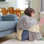 Una persona in casa con coperta e guanti attaccata al termosifone