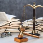 dei libri di legge sullo sfondo e davanti una bilancia di giustizia ed un martello da giudice