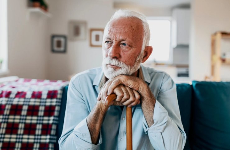 anziano seduto appoggiato al bastone con espressione triste