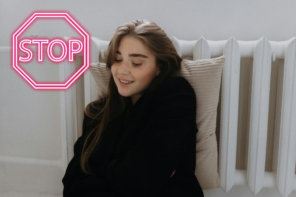 Una persona sdraiata su un termosifone ed un segnale di stop in alto a sinistra