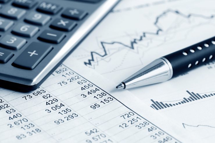 Un foglio di conti e grafici su cui poggiano una penna ed una calcolaltrice