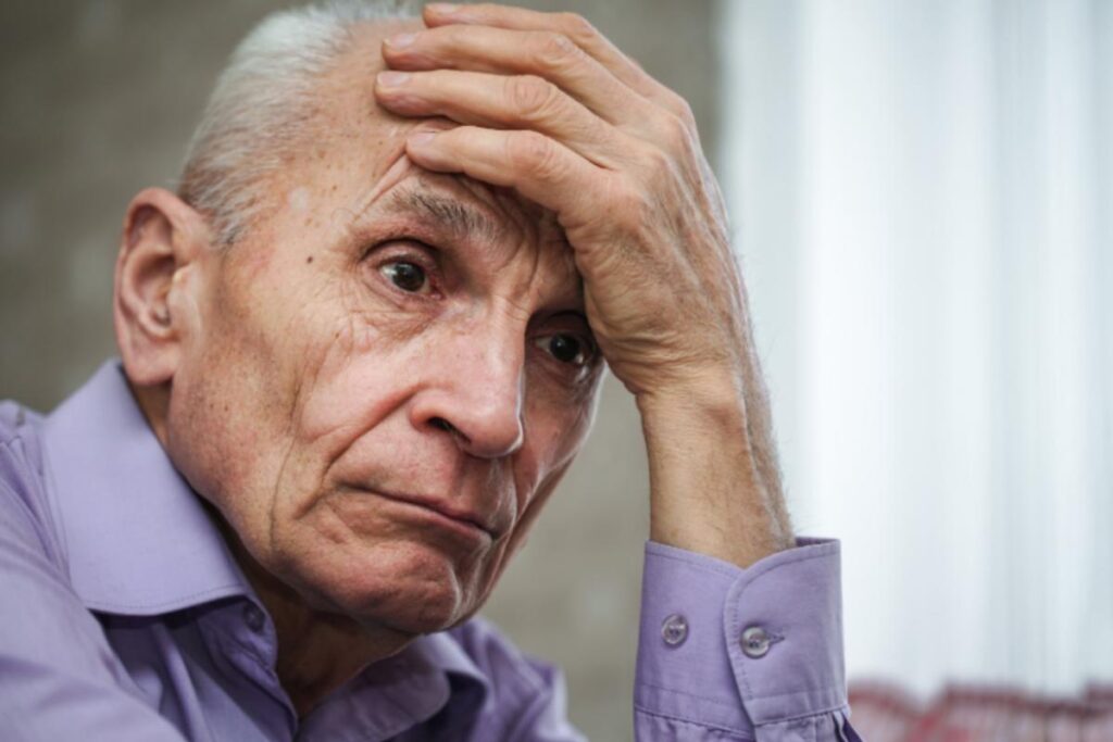 uomo anziano triste con una mano sulla fronte