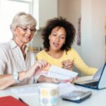 due donne che sorridono mentre leggono una bolletta davanti al computer