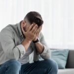 uomo seduto sul divano con la mani che coprono la faccia