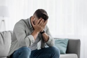uomo seduto sul divano con la mani che coprono la faccia